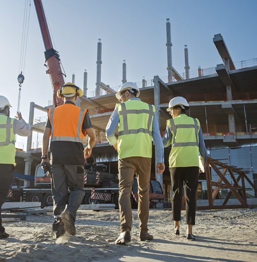 Diverse Team of Specialists Inspect Commercial, Industrial Building Construction Site. Real Estate Project with Civil Engineer, Investor and Worker. In the Background Crane, Skyscraper Formwork Frames